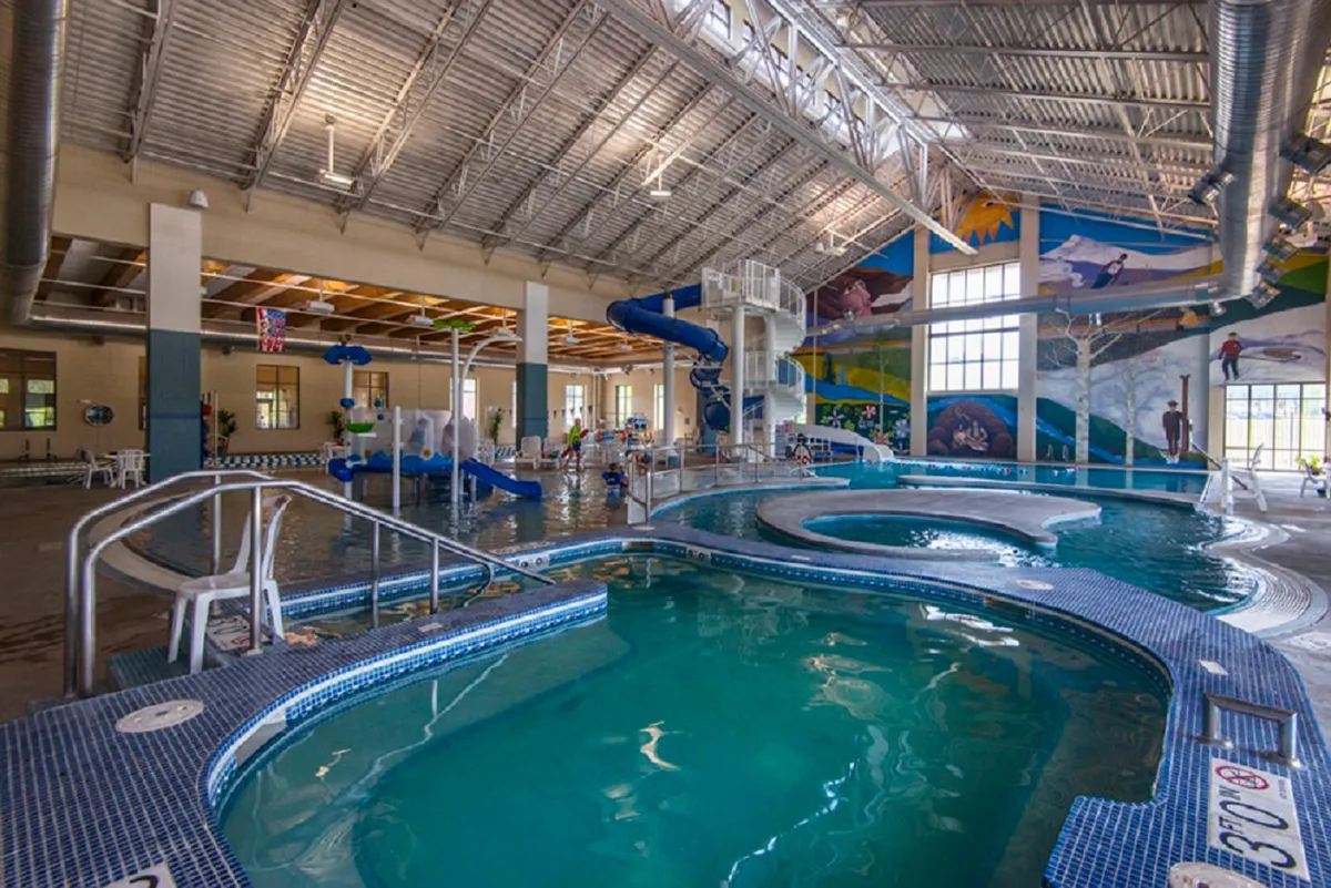 A lively indoor pool area featuring colorful water slides and a swimming pool, where children are actively playing and families are gathered. The mural and bright environment convey fun and energy, perfect for family outings and recreation.