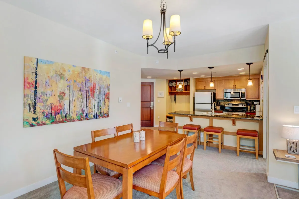 A welcoming dining table adjacent to a kitchen bar area, with colorful artwork adding warmth and personality to the space. The area is set for entertaining guests or enjoying family dinners, capturing the sense of celebration and connection emphasized in the section.