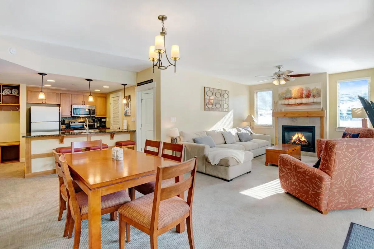 The image showcases a warm, open-concept living space with a stylish dining table, plush sofa, inviting fireplace, and modern kitchen area. The scene exudes coziness, perfect for gathering with loved ones, sharing stories by the fire, and enjoying homemade meals together.